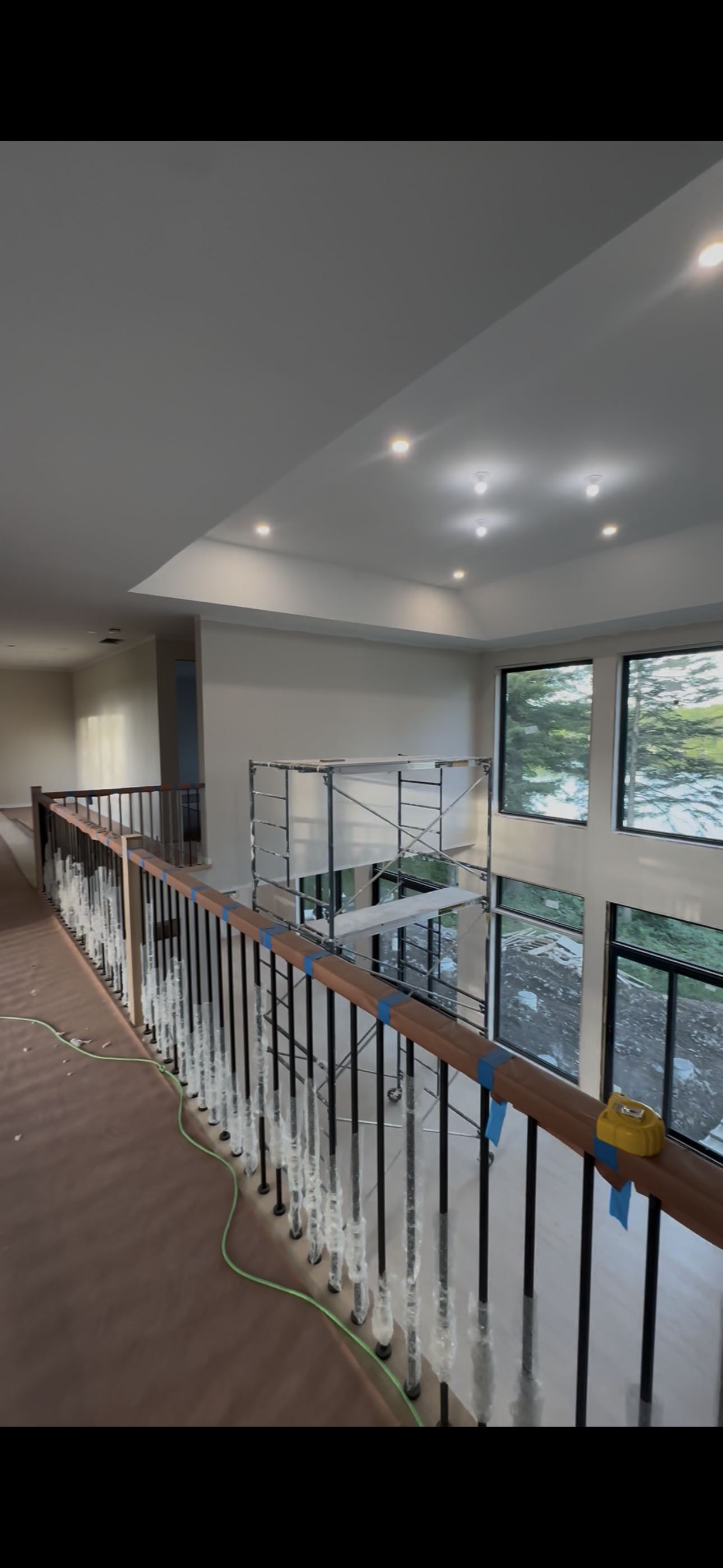 New build finishing — upper hallway drywall complete, iron railing being installed