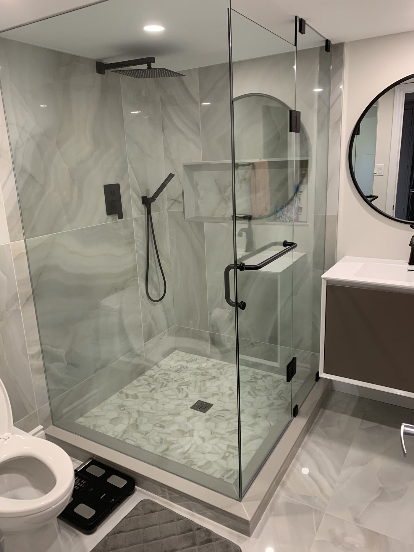 Bathroom renovation — marble walk-in shower, mosaic tile floor, black fixtures, round mirror