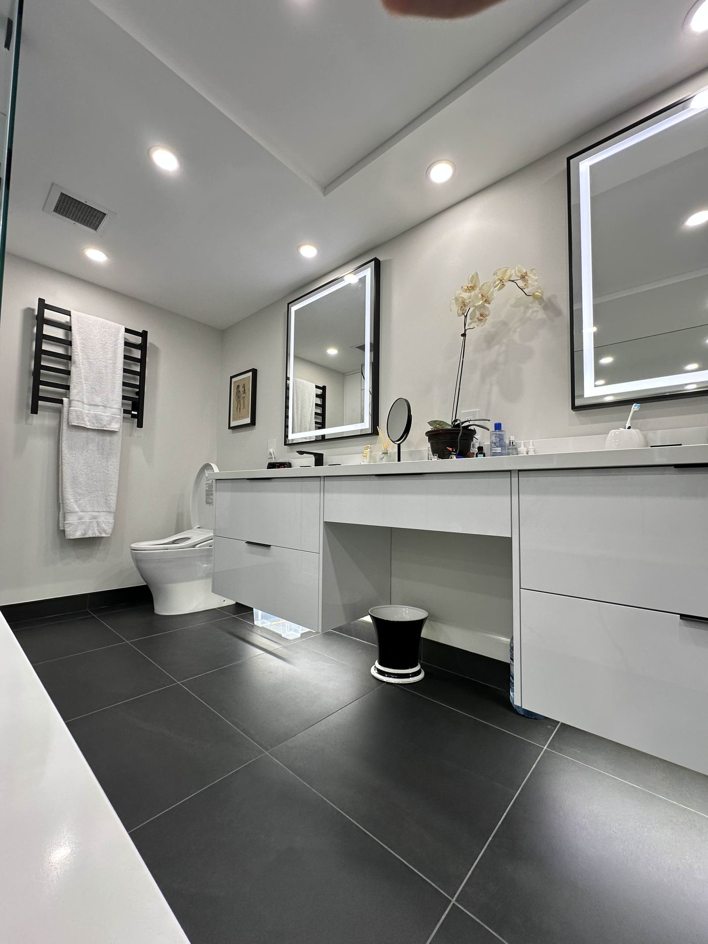 Bathroom renovation — white gloss floating vanity, dark tile floor, LED mirrors