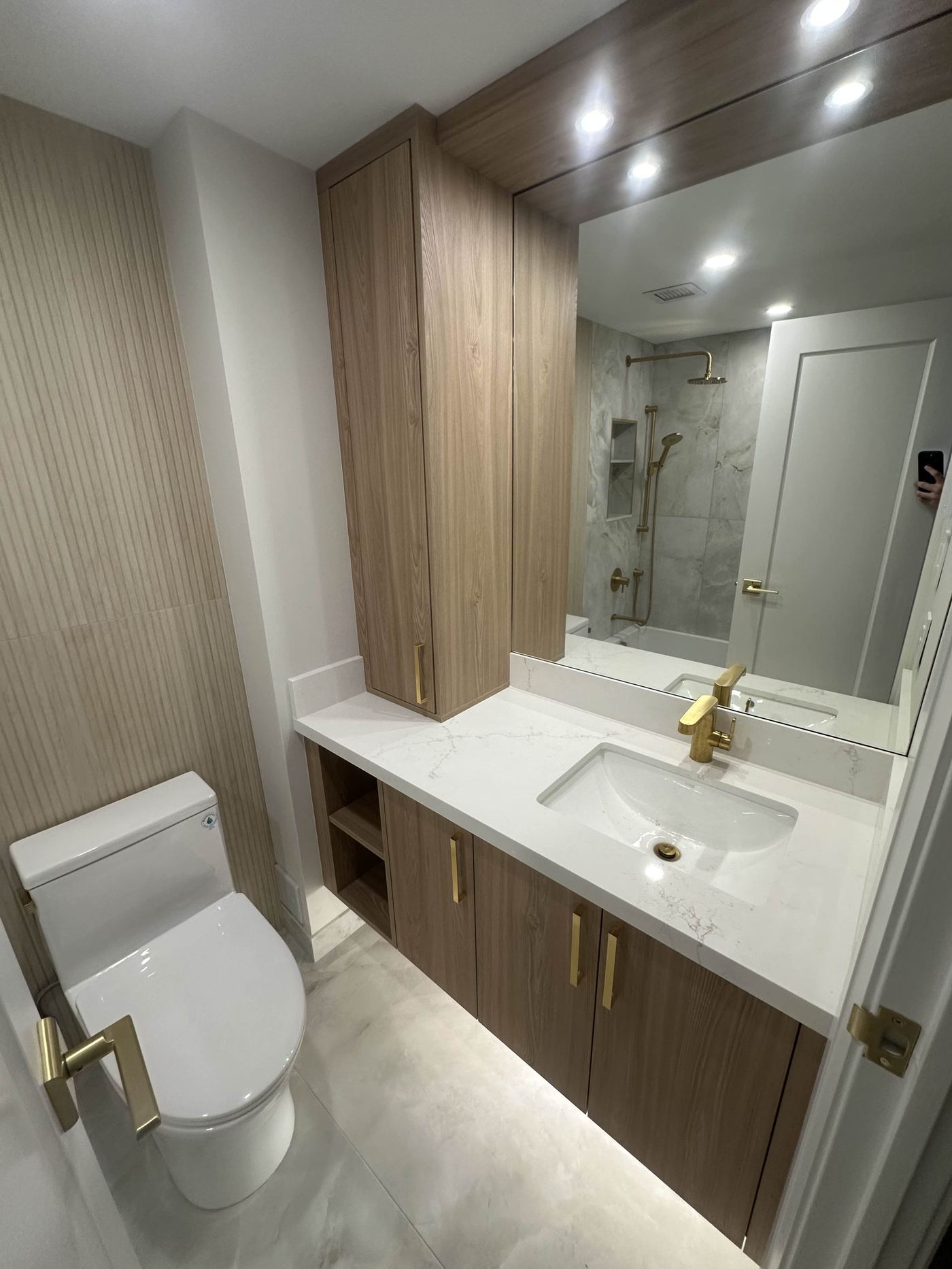 Bathroom renovation — wood vanity, gold fixtures, marble shower