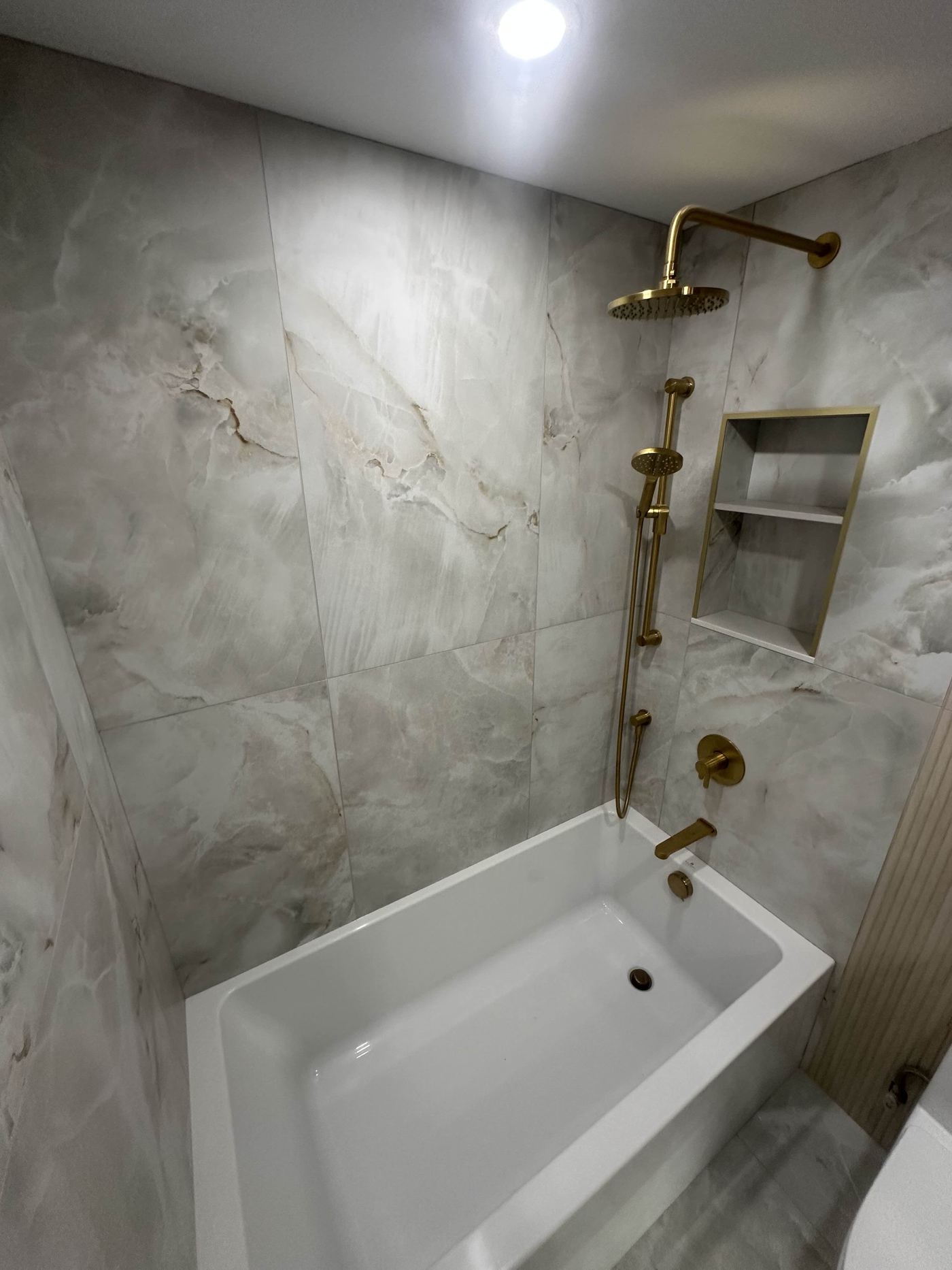 Bathroom renovation — marble tile surround, gold rain shower, soaker tub