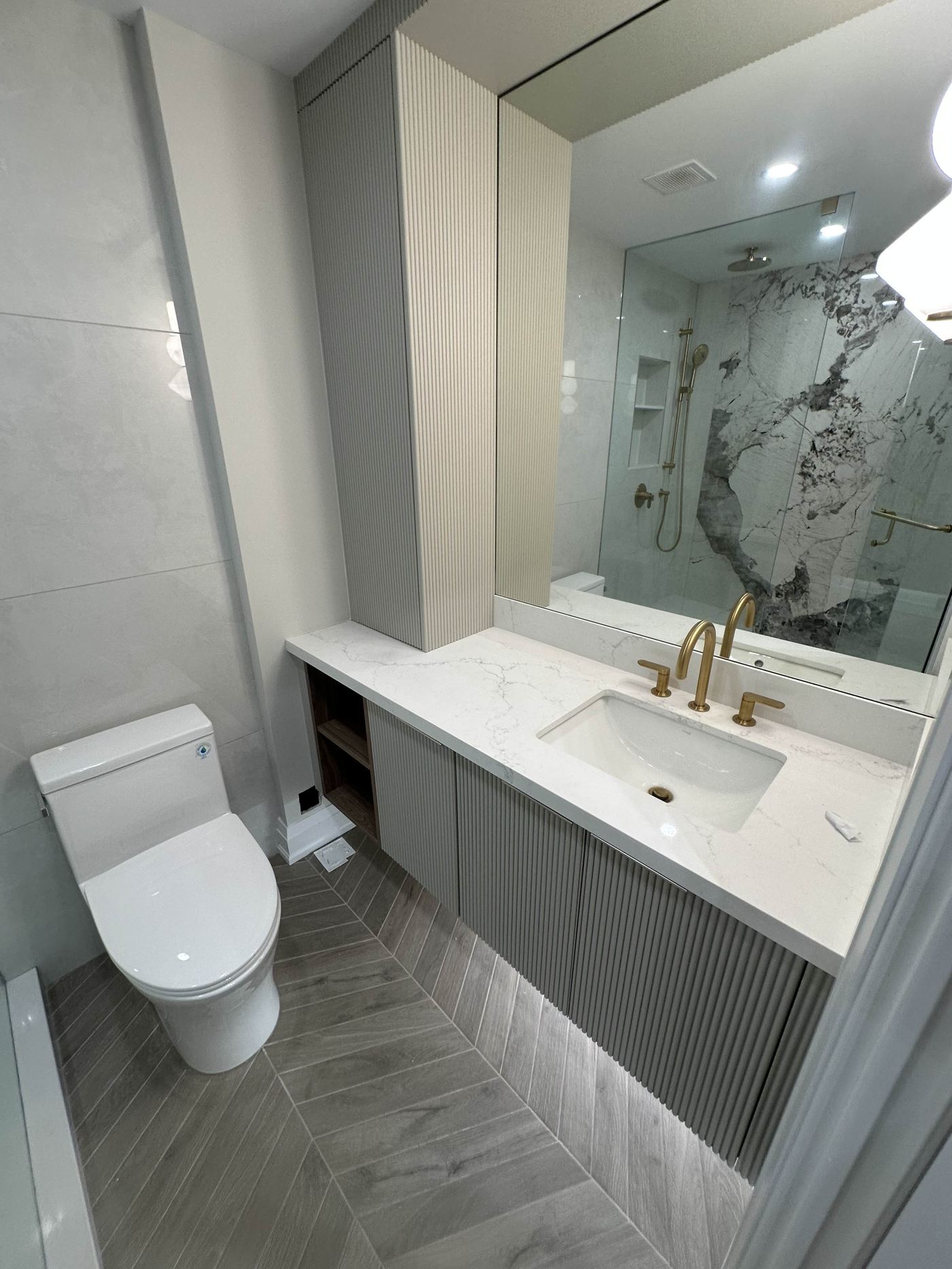 Bathroom renovation — grey ribbed floating vanity, gold fixtures, marble shower
